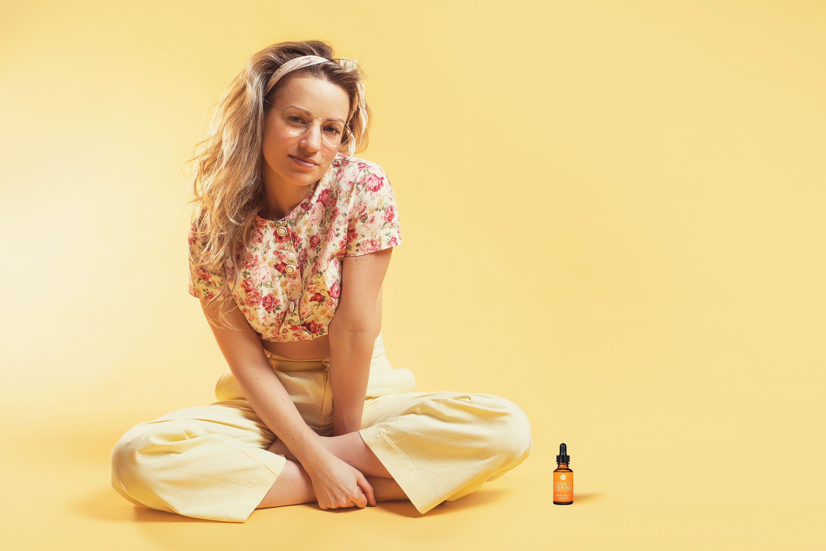 Woman sitting on a yellow background with a bottle of vitamin c